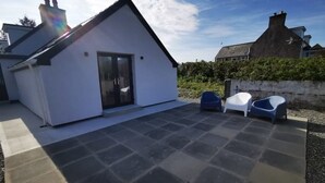 Ein modernes Haus mit gefliestem Patio, einer Schiebetür aus Glas und zwei Plastikstühlen.