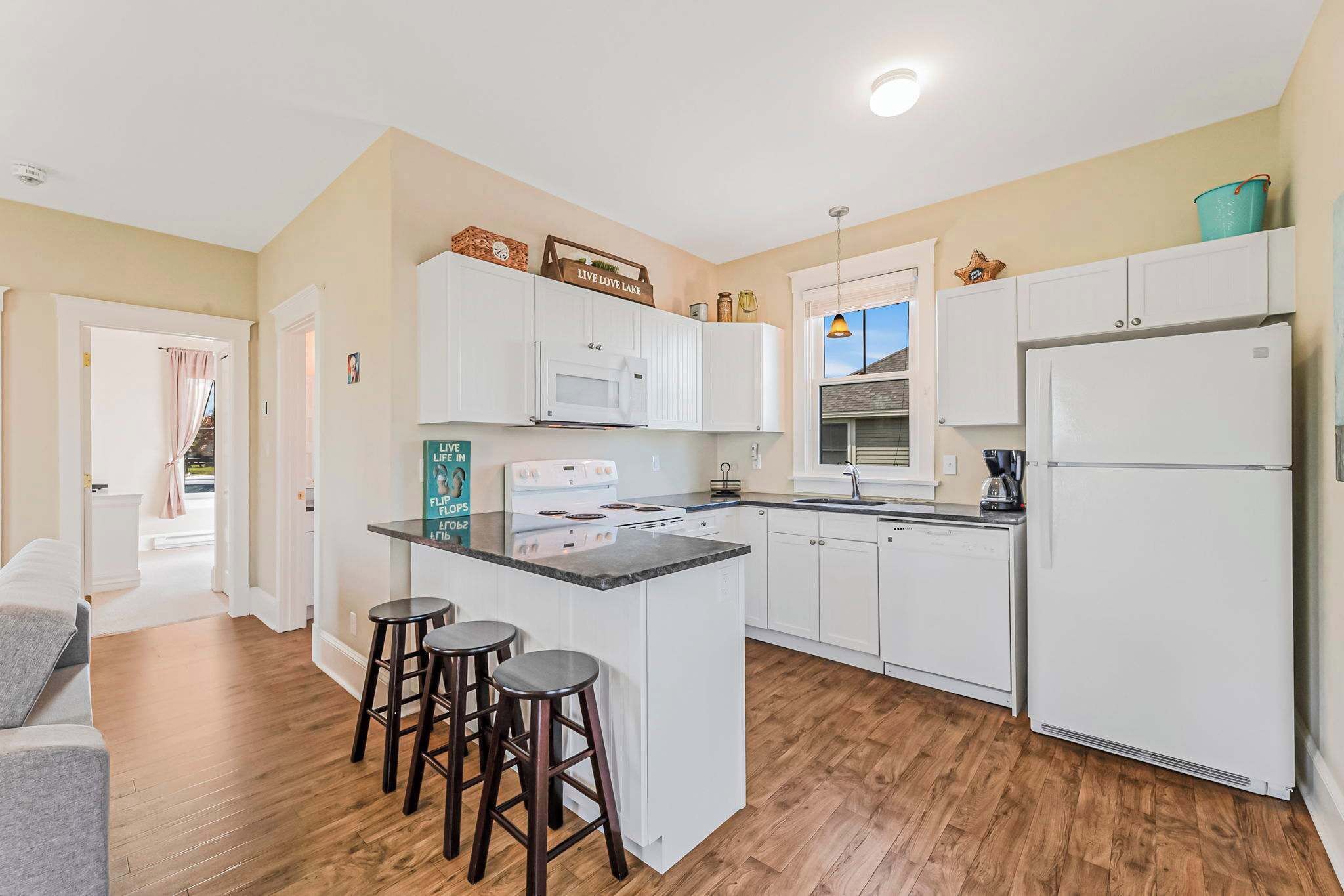 A modern kitchen with white cabinets, a central island with stools, a refrigerator, and a window with a view.