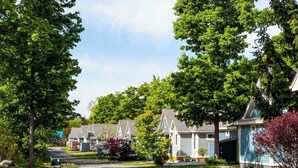 Une rue résidentielle bordée de maisons et d’arbres, avec un ciel dégagé.