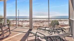A room with large windows overlooking a beach, wooden flooring, and several metal chairs. - 🌊Beach View-2 Beachfront Screened Decks-4BR-Windchimes🌊 (Mexico Beach)