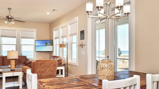 A spacious living area with a wooden dining table, white chairs, a brown sofa, and a ceiling fan. - 🌊Beach View-2 Beachfront Screened Decks-4BR-Windchimes🌊 (Mexico Beach)