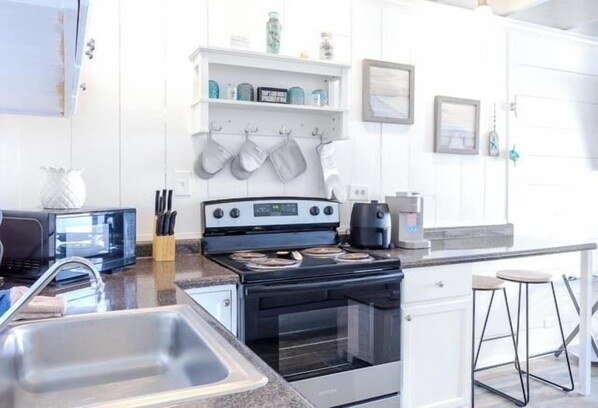 Cocina moderna con estufa, microondas y lavabo. Hay taburetes de bar y una cafetera en la encimera.
