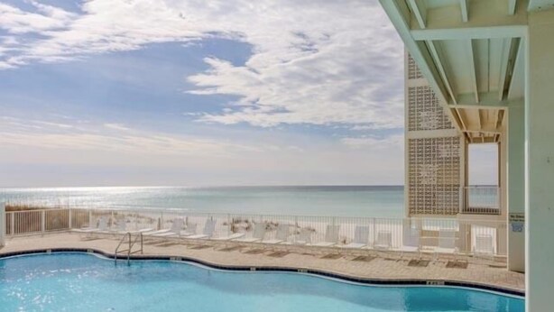 A pool with a view of the ocean, lounge chairs, and a covered area with a patterned wall.