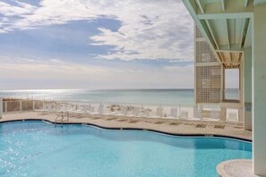 Una piscina con vista al océano, sillas de descanso y una zona techada con un muro decorado.