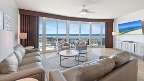 A spacious living room with a large window, a ceiling fan, and a flat-screen TV.
