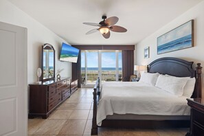 A bedroom with a bed, a ceiling fan, a TV, a dresser, and a view of the ocean.