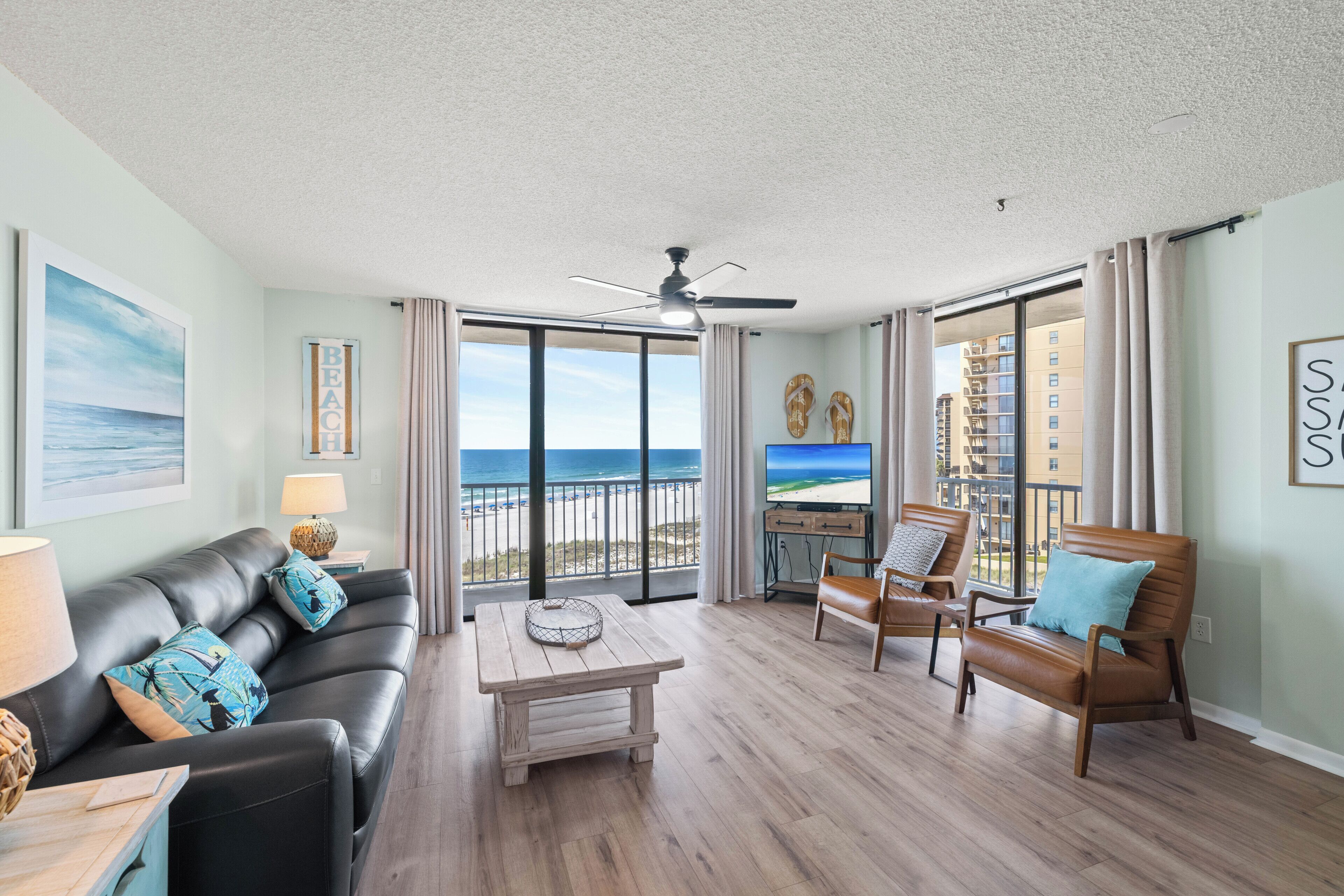 A living room with a view of the beach, a ceiling fan, and a wooden coffee table.