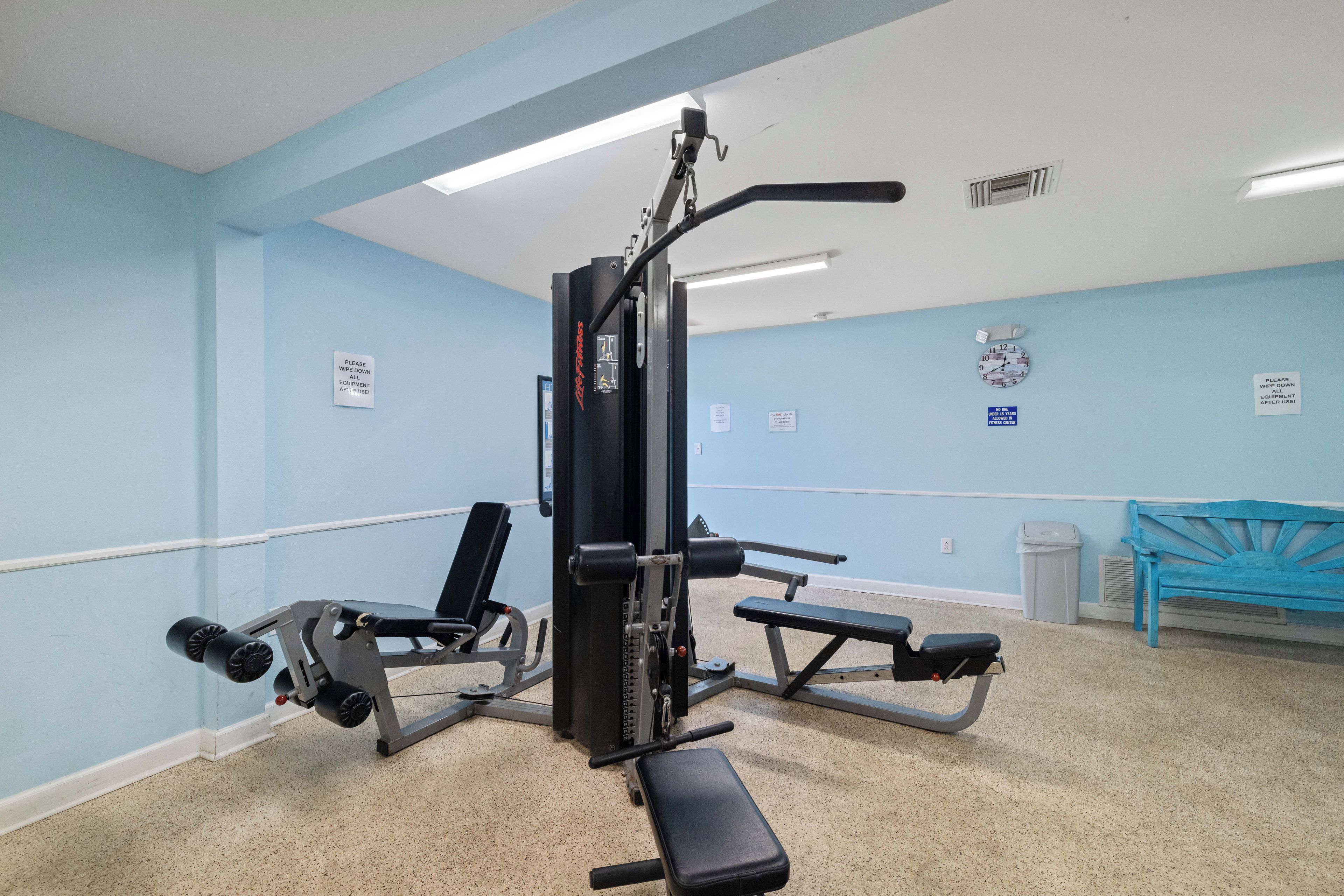 Une salle de sport équipée de matériel d’exercice, d’une horloge et d’un banc.
