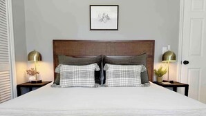 Una cama bien hecha con un juego de almohadas a cuadros, un cabecero de madera y dos lámparas de noche.