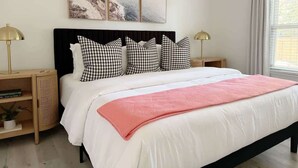 Une chambre à coucher avec un lit, des tables de chevet, une fenêtre et un tableau accroché au mur.