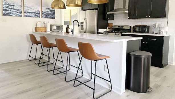 Une cuisine moderne dotée d’un îlot central, de tabourets de bar et de luminaires suspendus.