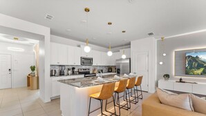 Une cuisine moderne avec des meubles blancs, un îlot central doté de tabourets, des appareils en acier inoxydable et un éclairage suspendu.