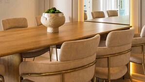 Un espace repas moderne avec une table en bois, des chaises recouvertes d’un tissu beige et une plante placée au centre.