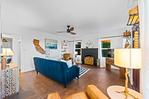 A modern living room with a blue sofa, a fireplace, a ceiling fan, and a TV. - Perfect 4 Families, Walk 2 Beach, Private Jacuzzi* (Oxnard)