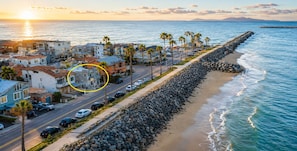 A coastal residential area with houses, a beach, and a rocky breakwater.