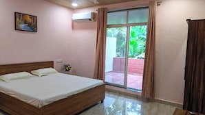 Quarto com cama de madeira, um quadro na parede, ar condicionado e vista para o verde através de uma porta deslizante.