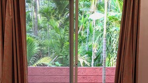 Quarto com uma grande porta de vidro deslizante que dá para um pátio de tijolos vermelhos com vegetação.