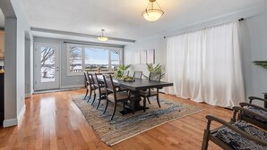 A dining area with a wooden table, chairs, and a rug. There are two pendant lights above the table.