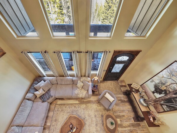 A spacious living area with a large sectional sofa, a coffee table, and a fireplace. There are multiple windows providing natural light and views of the outdoors.