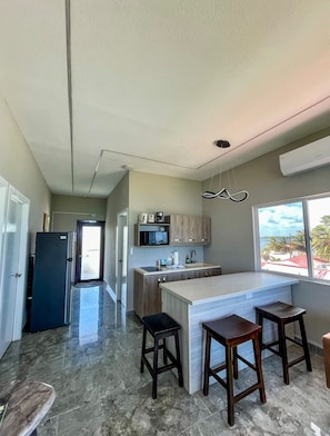 Una cocina moderna con una isla central, taburetes de bar y vistas al océano a través de un ventanal grande.