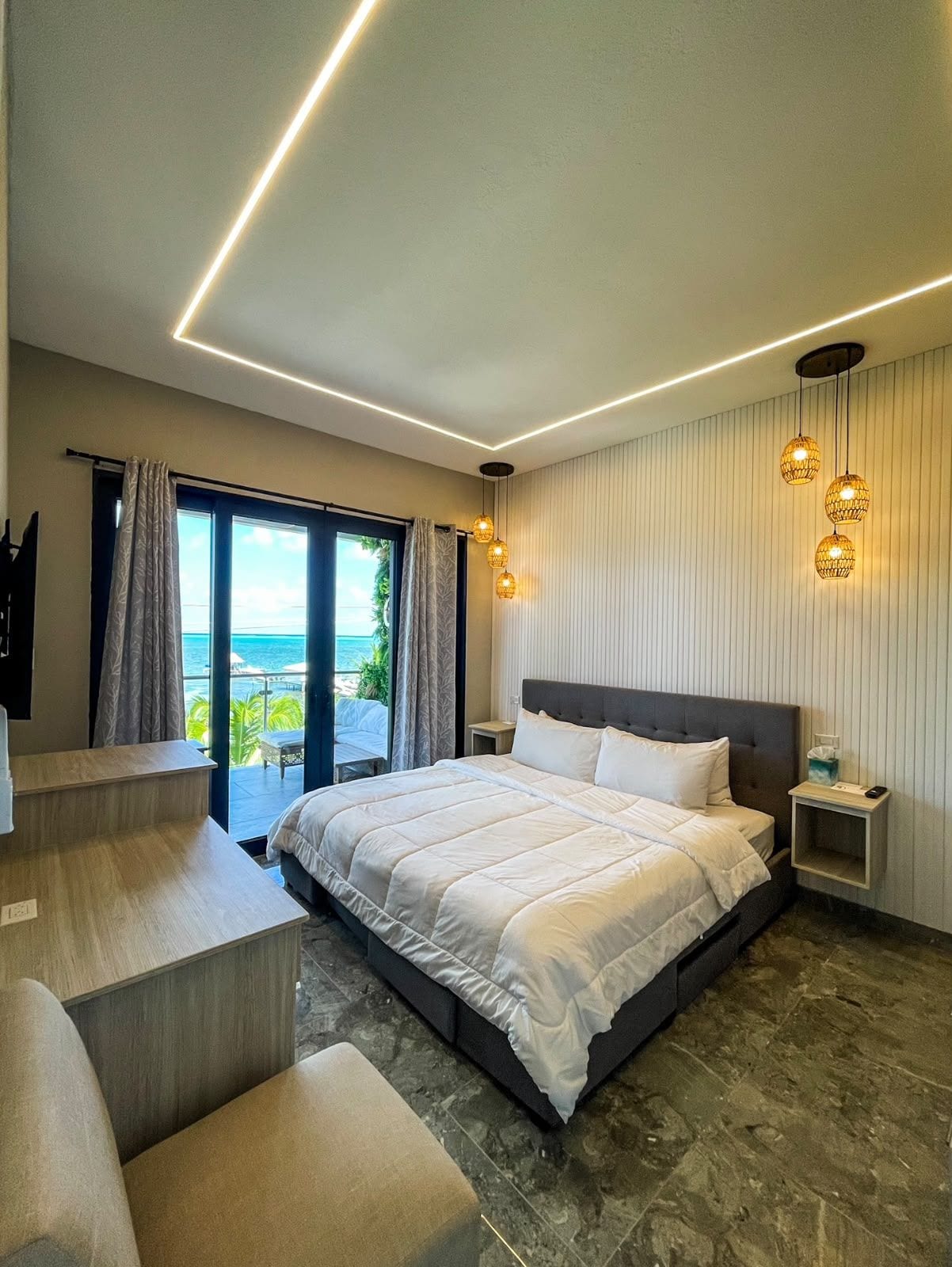 A modern bedroom with a large bed, a seating area, and a view of the ocean.