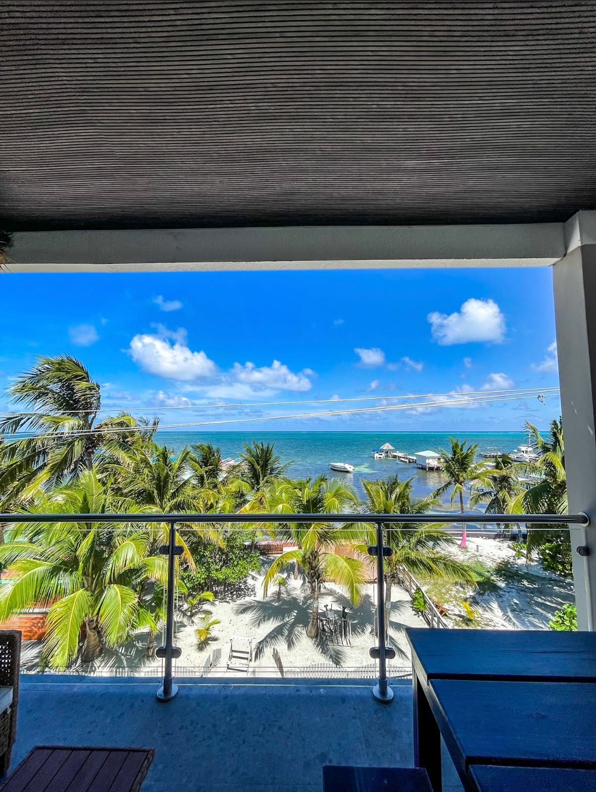 Un balcón con vista a una playa, palmeras y un cielo despejado.
