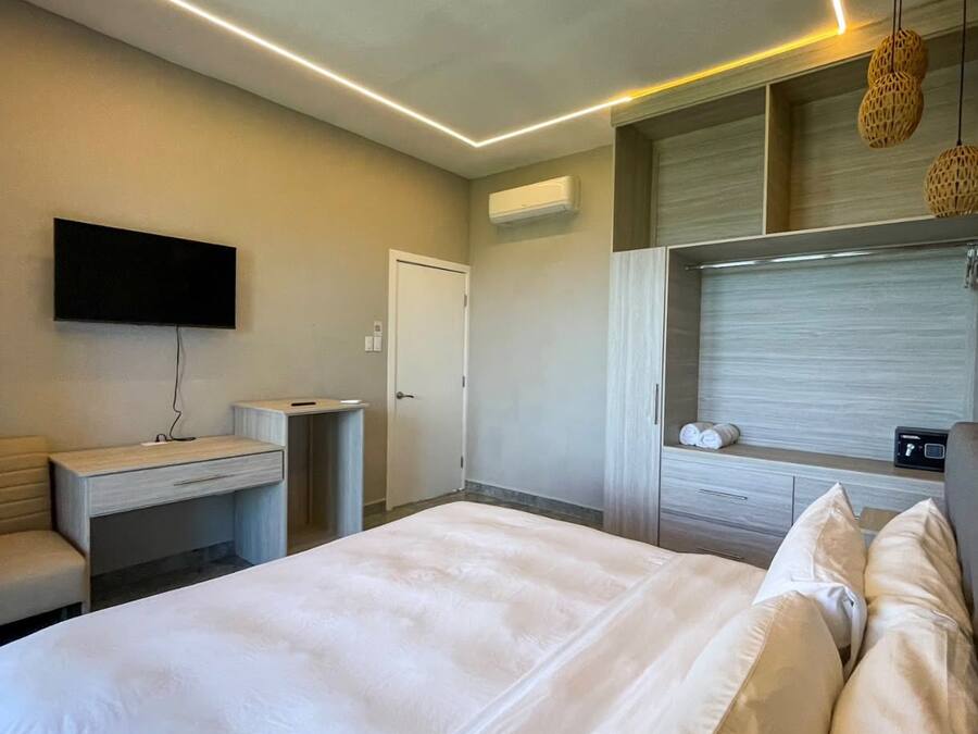 Una habitación de hotel moderna con una cama grande, un televisor de pantalla plana montado en la pared, un escritorio con una silla y un armario.