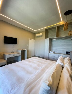 Una habitación de hotel moderna con una cama grande, un televisor de pantalla plana montado en la pared, un escritorio con una silla y un armario.