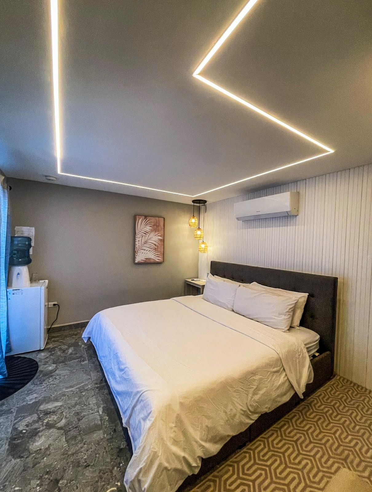 Une chambre d’hôtel équipée d’un lit, d’une table de chevet, d’un climatiseur mural et d’un distributeur d’eau.