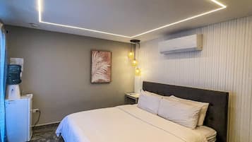 Ein Hotelzimmer mit Bett, Nachttisch, Wand-Klimaanlage und Wasserspender.