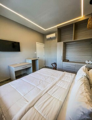 A modern bedroom with a bed, bedside tables, a wardrobe, and a wall-mounted air conditioner. - Caye Caulker Condos By Barefoot (Caye Caulker)