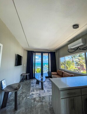 Una sala de estar moderna con vista al océano, un televisor de pantalla plana, un sofá, una mesa de centro y una zona de cocina.