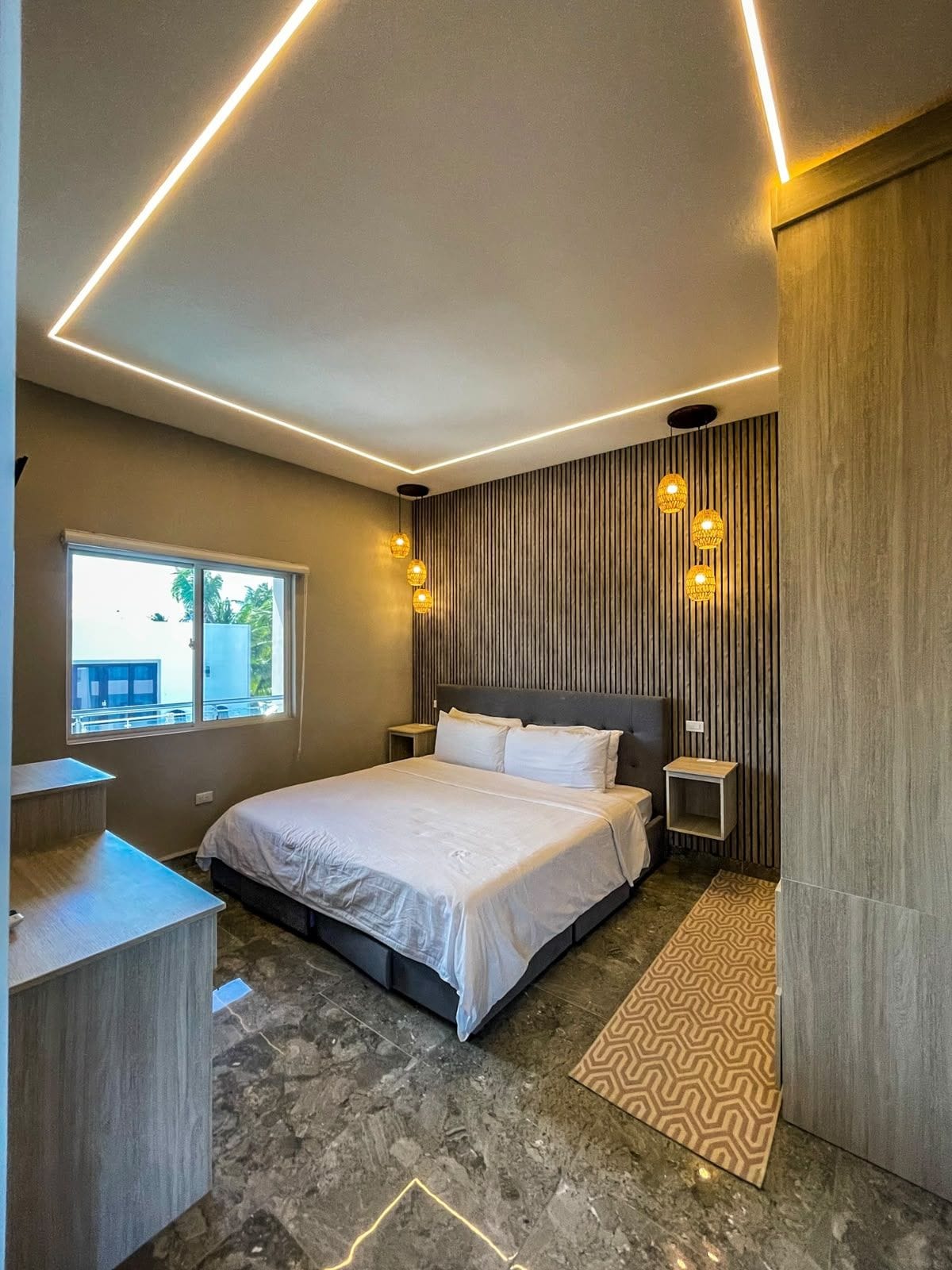 A modern bedroom with a large bed, bedside tables, a window, and a patterned rug.