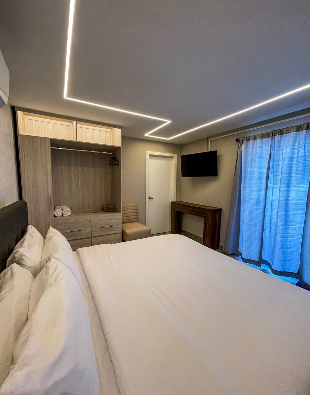 Habitación de hotel con cama, armario, televisor y ventana con cortinas.