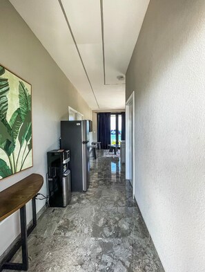 A hallway with a kitchen area, a dining table, and a view of the outside. - Caye Caulker Condos By Barefoot (Caye Caulker)