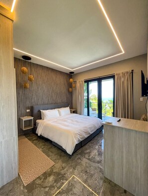 A modern bedroom with a bed, bedside tables, a desk, and a large window with curtains. - Caye Caulker Condos By Barefoot (Caye Caulker)
