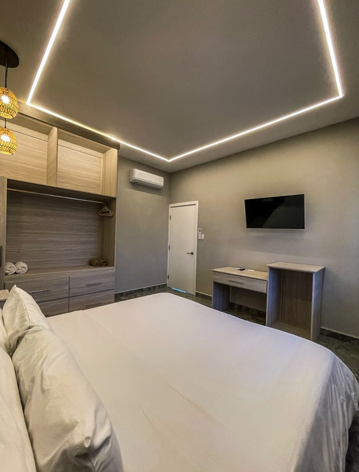 A modern bedroom with a large bed, built-in wardrobe, bedside table, and a mounted TV.