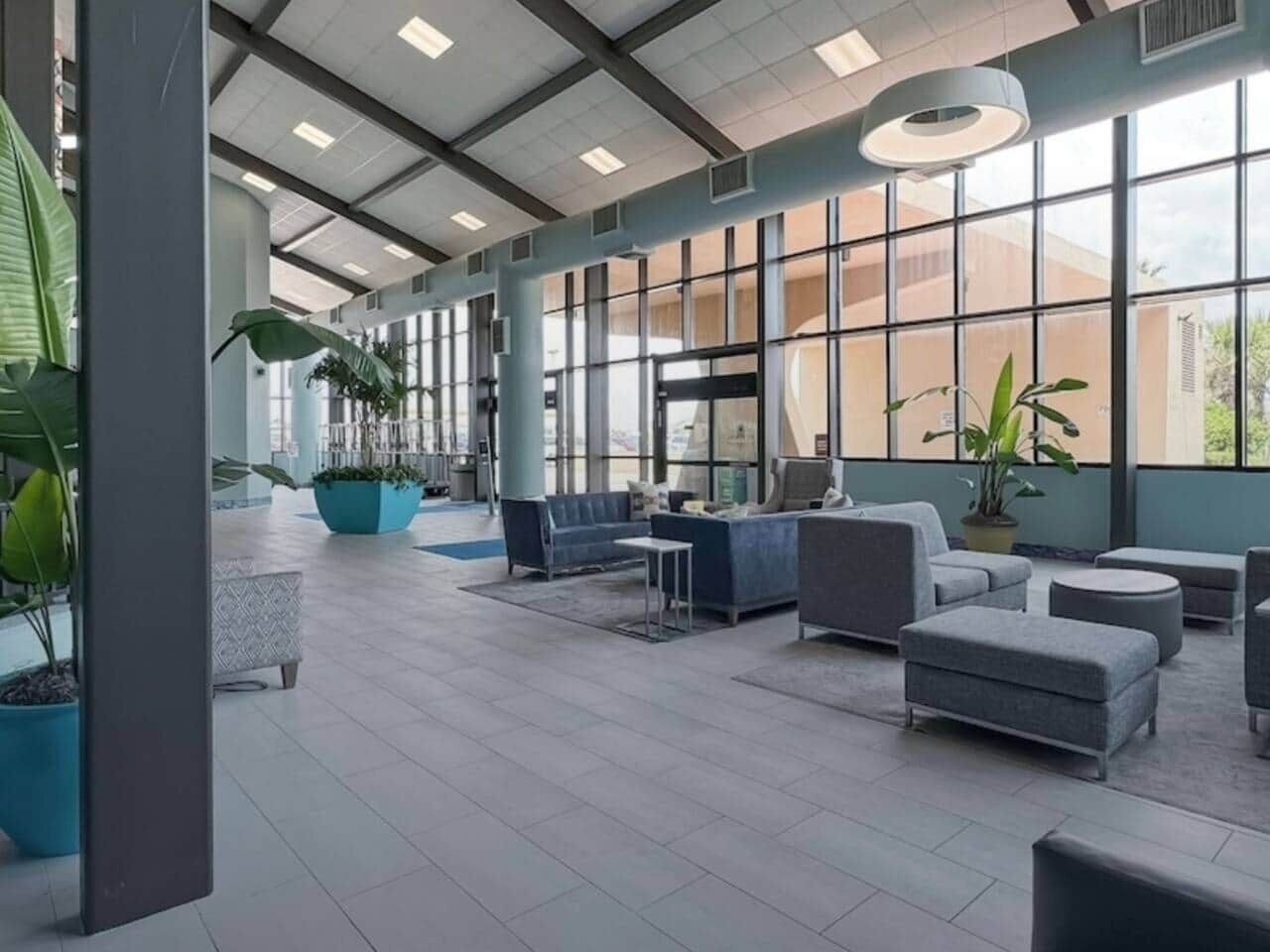 A spacious indoor area with large windows, seating arrangements, and potted plants.