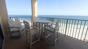 A balcony with a table and chairs, overlooking a beach with a railing. - Phoenix V Beachfront Family Condo with Pool and Gulf Views (Orange Beach)