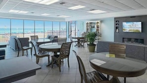 A modern office space with round tables and chairs, a large window offering a view of the city, and a television on the wall. - Phoenix V Beachfront Family Condo with Pool and Gulf Views (Orange Beach)