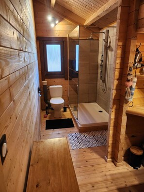 Ein kleines Badezimmer aus Holz mit einer Glasdusche, einer Toilette und einem Waschbecken.