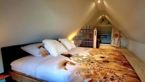 A bedroom with a sloped ceiling, a bed with floral bedding, a wooden headboard, and a small shelf with books and a lamp. - Cottage the Bird's Nest with jacuzzi (Oldekerk)