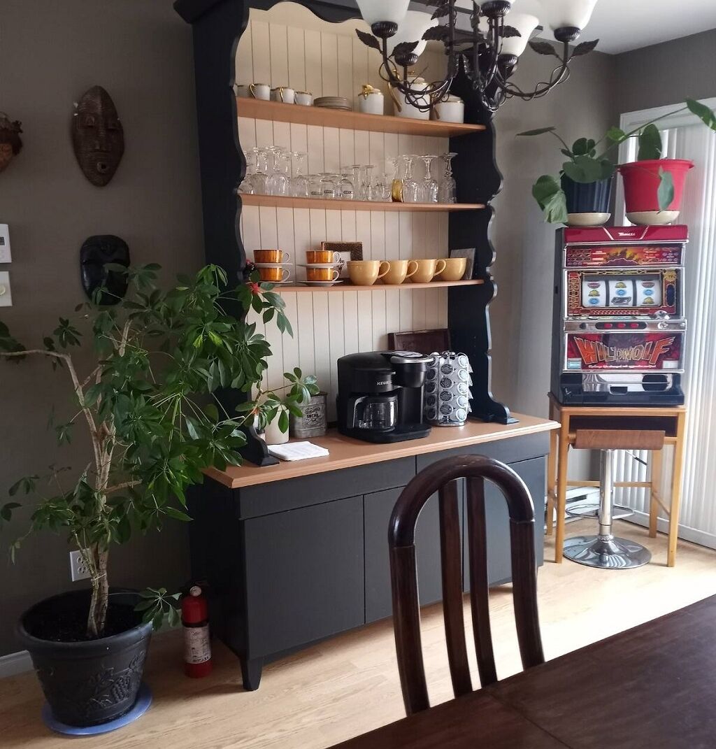 Une cuisine dotée d’un plan de travail en bois, d’une machine à café, d’une bouilloire et d’une étagère où sont rangés de la verrerie et des bols.