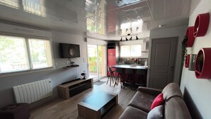 A modern living room with a sofa, coffee table, and TV. There's a kitchen area with a dining table and chairs. - Gîte 2 **, 55m², 2/4 persons, quiet, 20 min from the beaches Pornic, st Brévin (Vue)