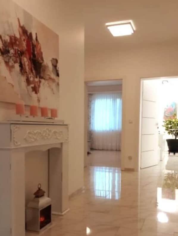 Un pasillo amplio con una chimenea blanca, un cuadro abstracto grande y una planta en maceta.