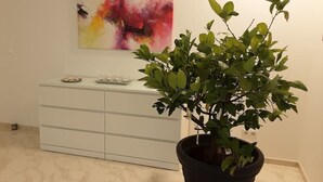 Une plante en pot, placée dans un coin, à côté d’une armoire blanche et d’un tableau abstrait aux couleurs vives accroché au mur.