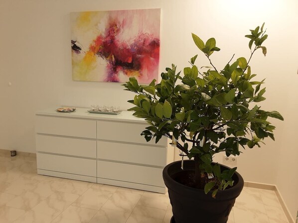 A potted plant in a corner with a white cabinet and a colorful abstract painting on the wall.