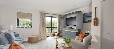 A modern living room with a sofa, armchair, and ottoman, a wooden coffee table, and a TV stand with a flat-screen TV.