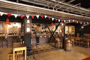 A bar with stools, a counter, and a person standing. There are tables and chairs in the foreground.