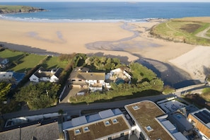 An aerial view of a coastal property with a sandy beach, a small cluster of houses, and a road leading to the beach. - Harlyn Folly- 100m from the beach - Parking (Harlyn Bay)